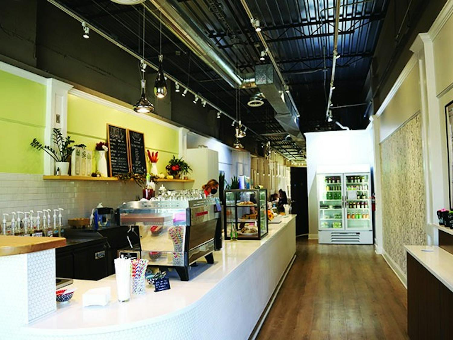 Blum Coffee's bar is brightly lit and located in the front of the store. The bar includes two large chalkboard menus and is lined with coffee machines, syrups and a case of baked goods.