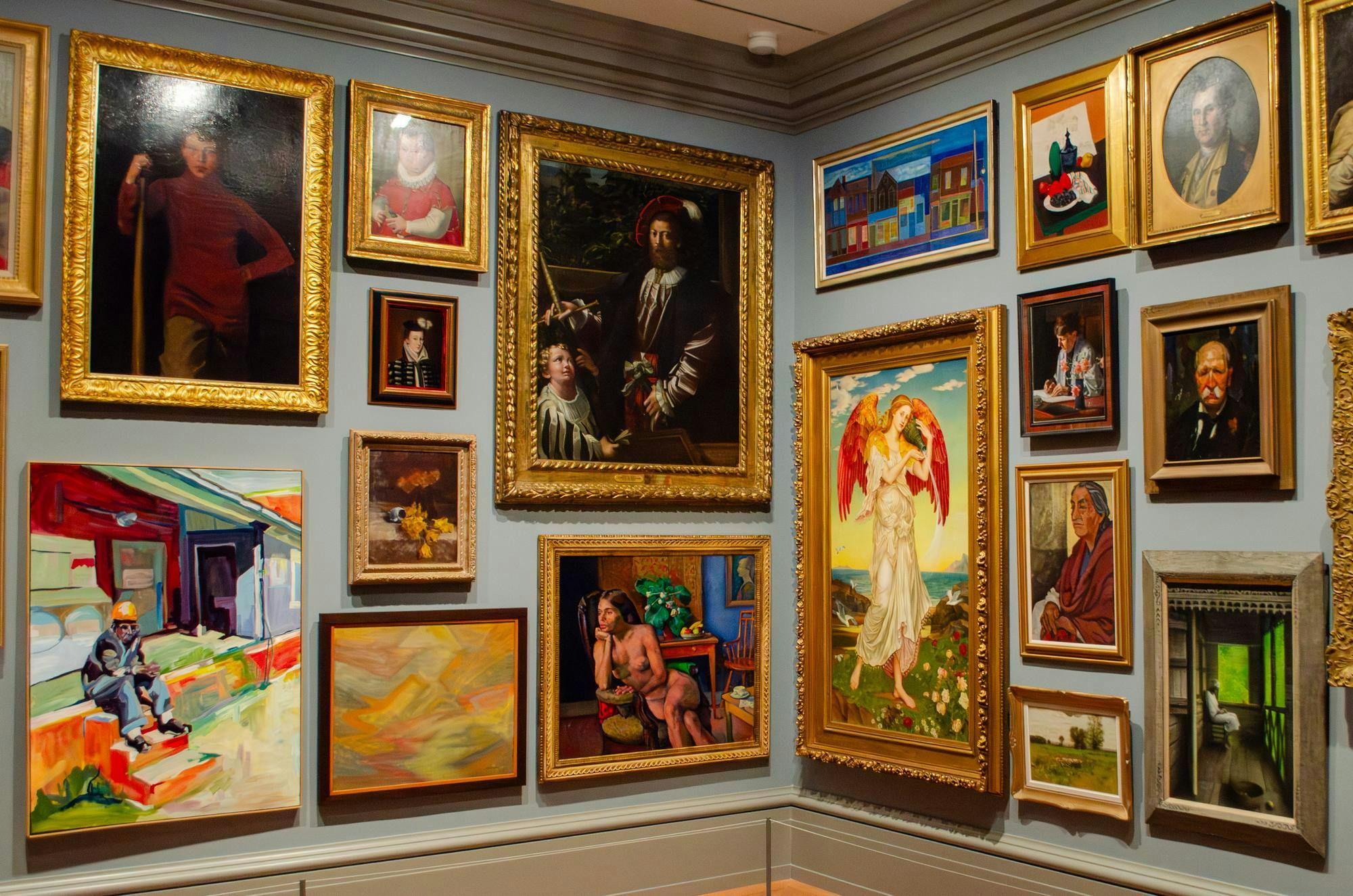 A collection of paintings hang on a wall at the Columbia Museum of Art. They are of various subjects and styles, and all have different frames.