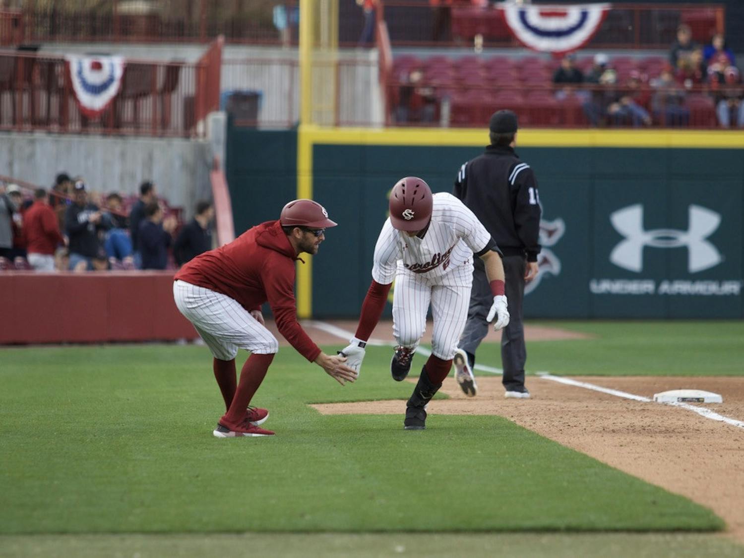 Fifth-year infielder Will McGillis heads into home plate and shares a high five with third base coach Scott Wingo. McGillis helped the Gamecocks to their 20-3 victory over UMass Lowell on Feb. 17, 2023. &nbsp;