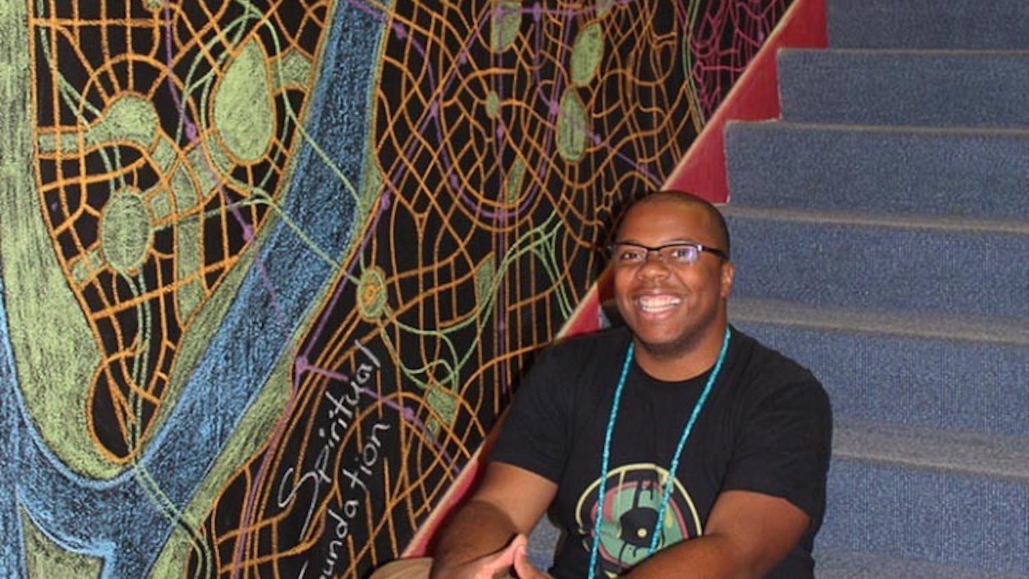 Michael Dantzler sits next to his mural, “Transcend Map,” which is a temporary mural he made in October 2016 for the University of South Carolina School of Music’s library.