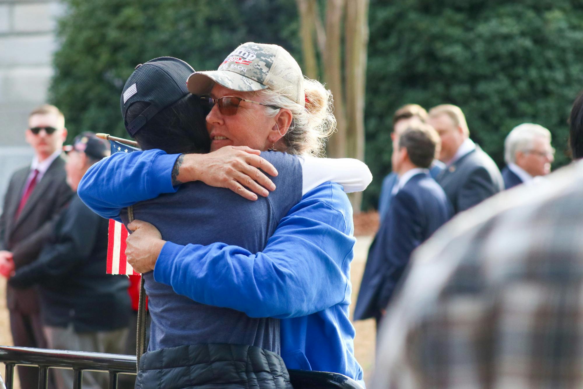 Kelli Powell, a representative of World Wide South Carolina on Telegram, hugs a friend over the fence before she enters the Statehouse for Trump's speech on Jan. 28, 2023. Powell was not one of the 500 that got access to the private event, however, she stayed out on the Statehouse lawn and enjoyed her personal "Jesus juice."