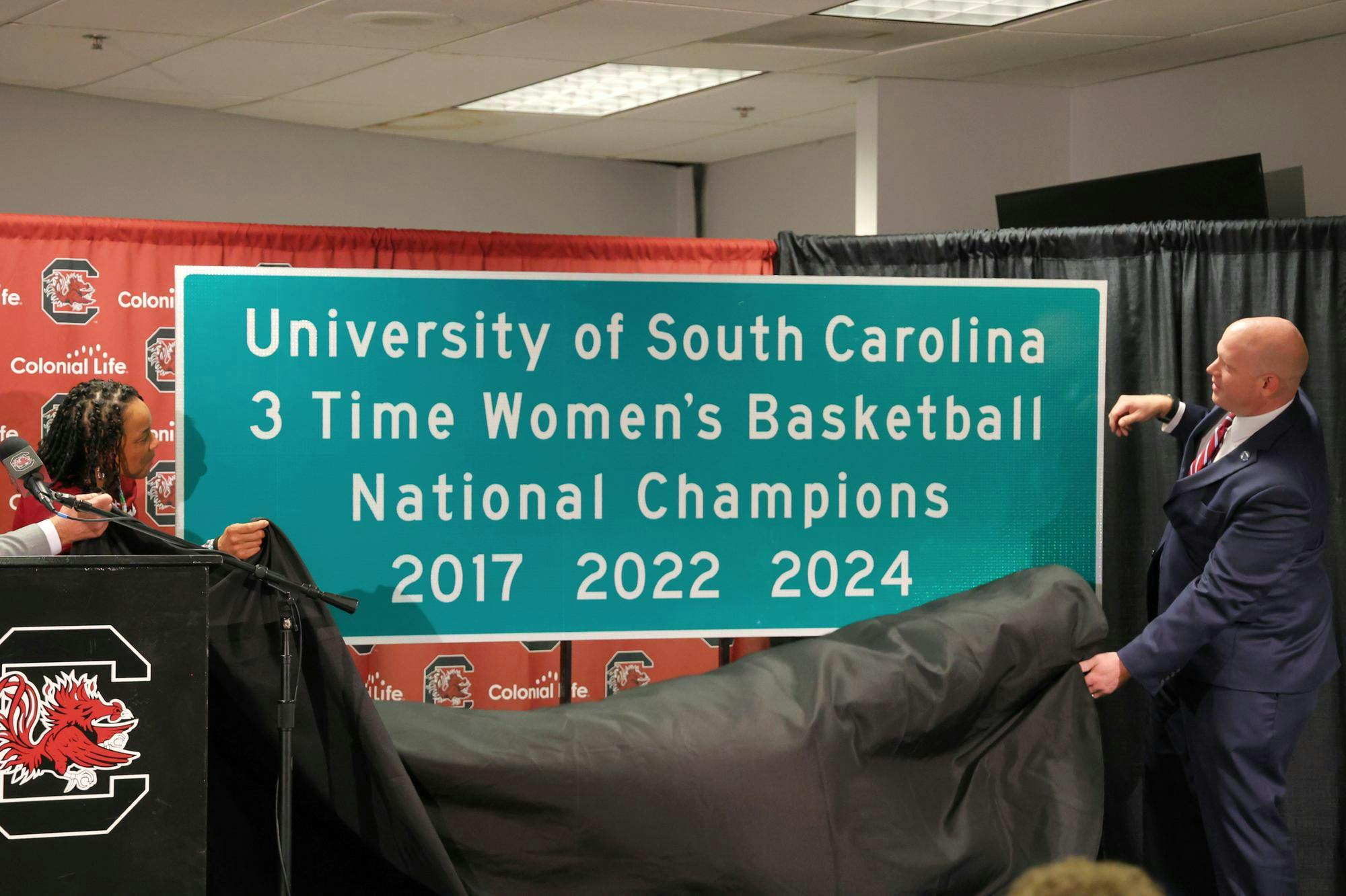 Head women's basketball coach Dawn Staley (left) and South Carolina Secretary of Transportation Justin Powell (right) unveil a new highway sign at Colonial Life Arena on Aug. 27, 2024, that honors the 2024 women's basketball national championship win. The state will put up 15 commemorative signs around Columbia and other parts of South Carolina.