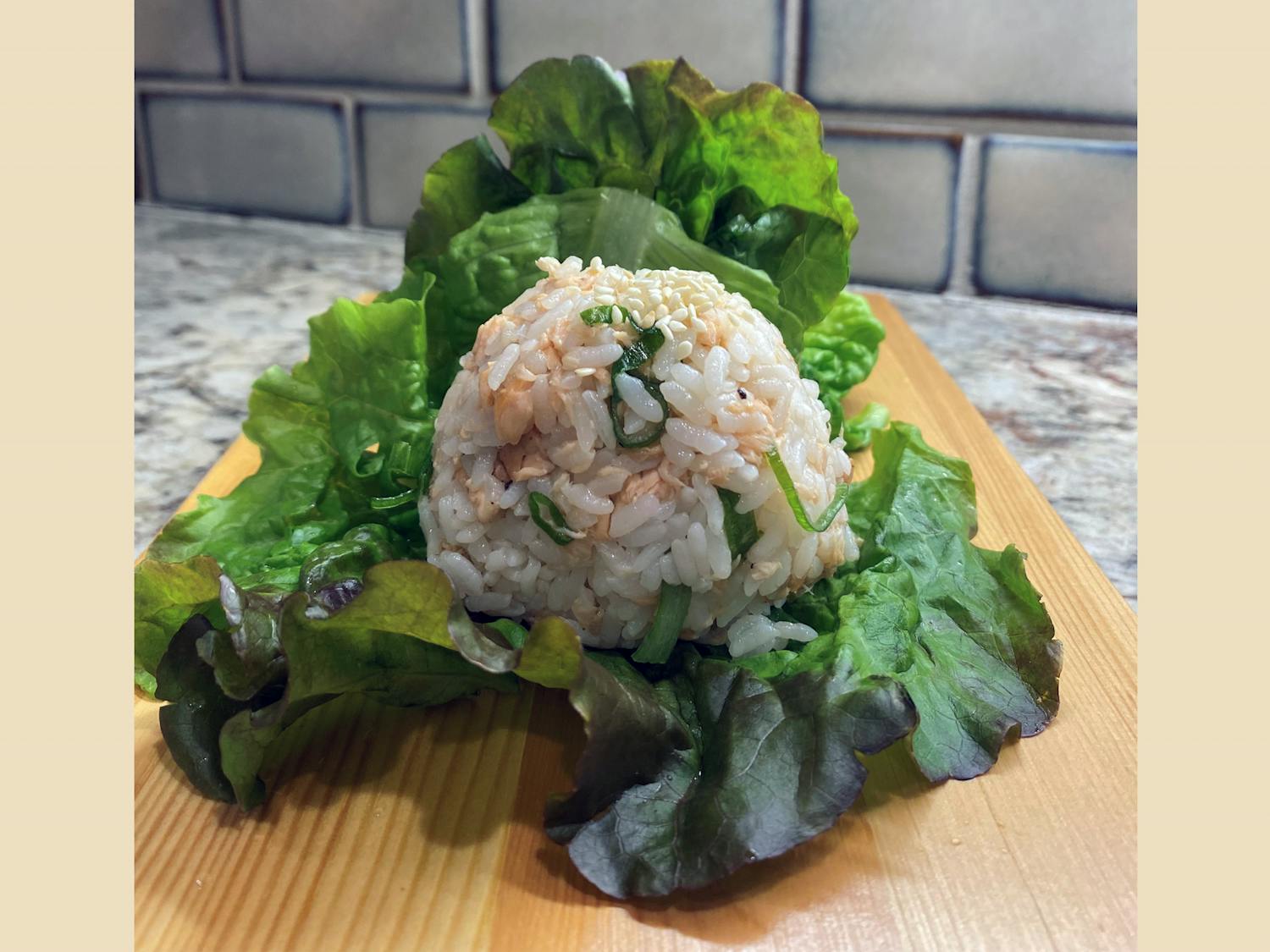 A rice ball made with sweet and savory salmon plated on a leaf of lettuce. Salmon rice balls are a quick and easy meal and perfect of a college student.