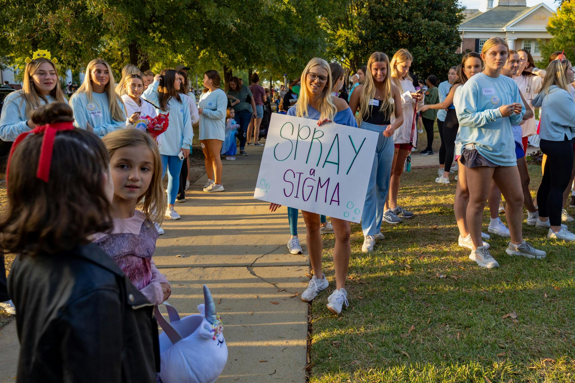 A Trick or Treat with the Greeks attendee member holds a sign reading "Spray Sigma" towards community members on Oct. 25, 2022. Trick or treaters and community members participated in spraying water at a small group of fraternity brothers dressed as mermaids as a way of entertaining attendees outside of the fraternity house.