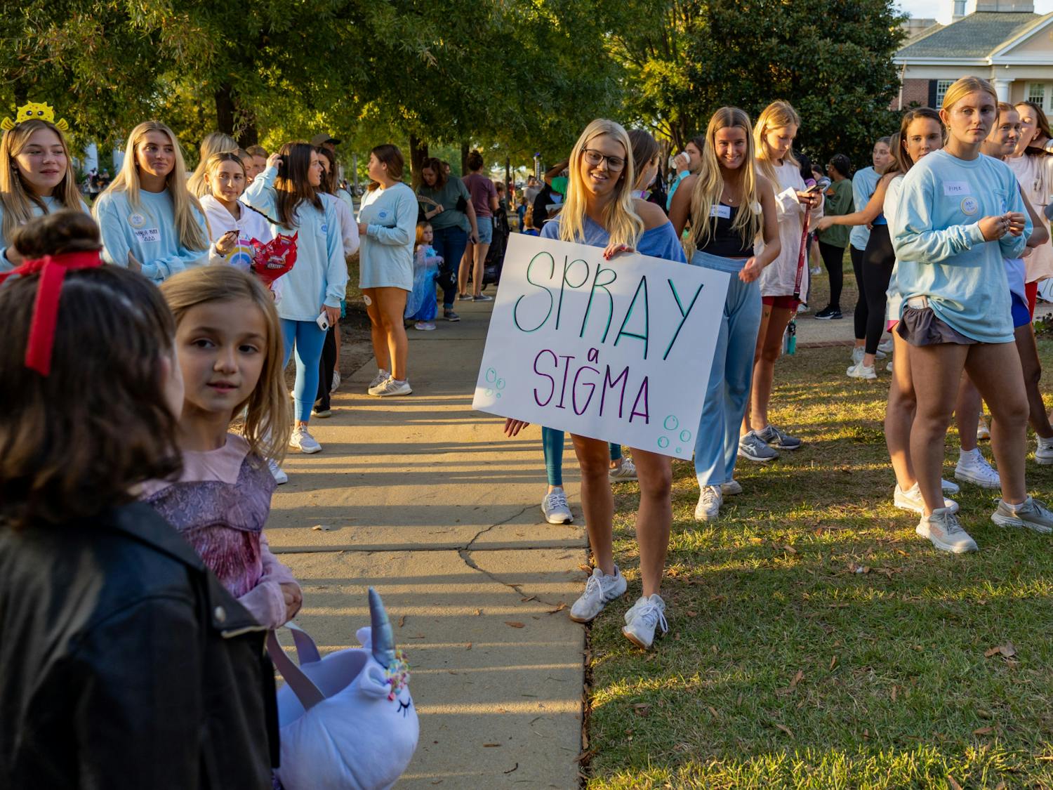 A Trick or Treat with the Greeks attendee member holds a sign reading "Spray Sigma" towards community members on Oct. 25, 2022. Trick or treaters and community members participated in spraying water at a small group of fraternity brothers dressed as mermaids as a way of entertaining attendees outside of the fraternity house.