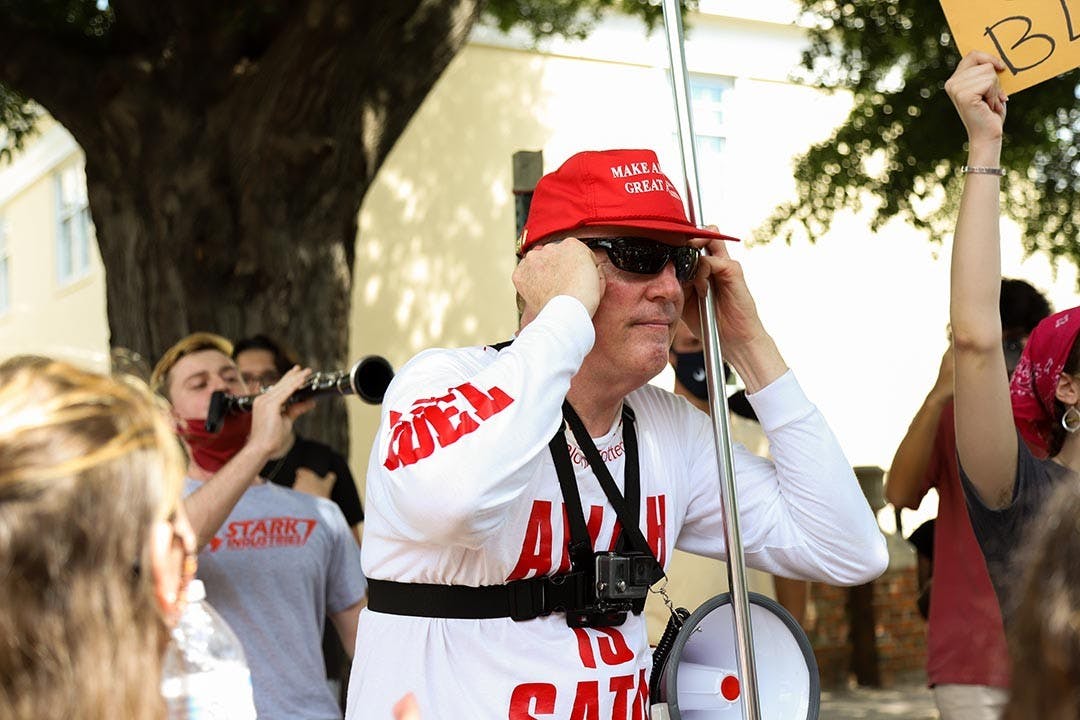 Jim Gilles covers his ears while a student with an instrument plays loudly. There were multiple students sporting instruments and playing when Jim Gilles was talking.