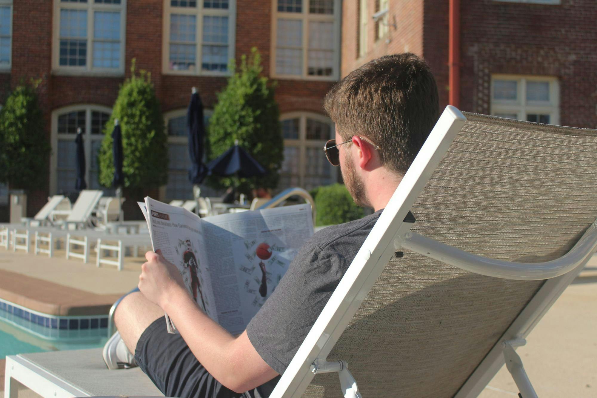 A photo of a person relaxing by the pool and reading the latest print edition of The Daily Gamecock newspaper.