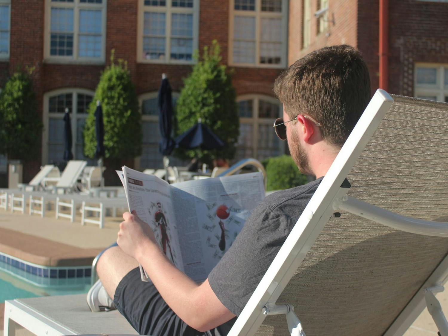 A photo of a person relaxing by the pool and reading the latest print edition of The Daily Gamecock newspaper.
