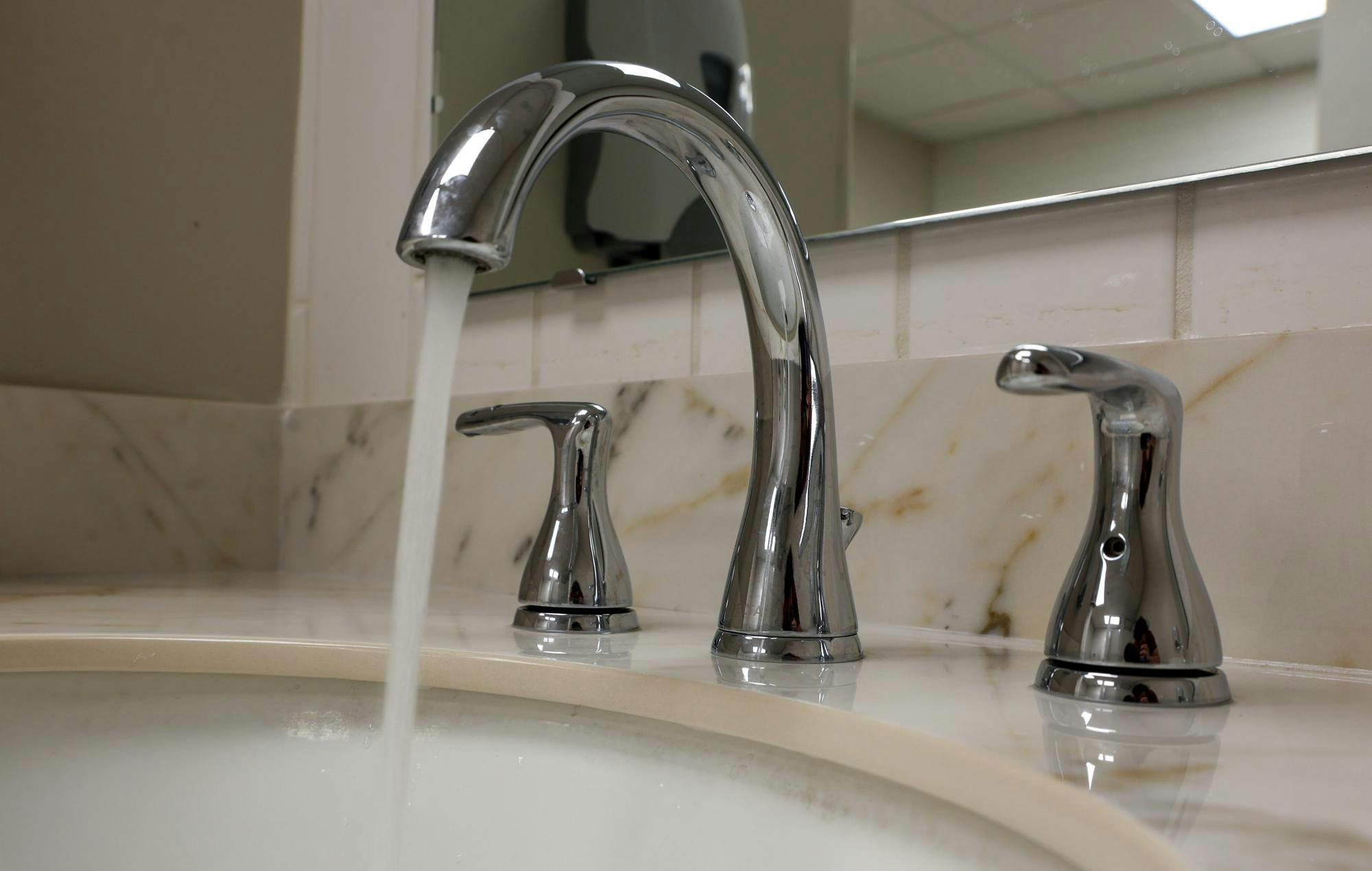 Water flows steadily from a chrome bathroom faucet into a sink beneath a mirror.