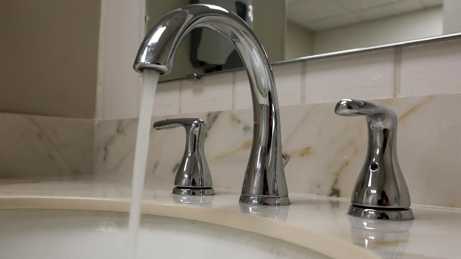 Water flows steadily from a chrome bathroom faucet into a sink beneath a mirror.
