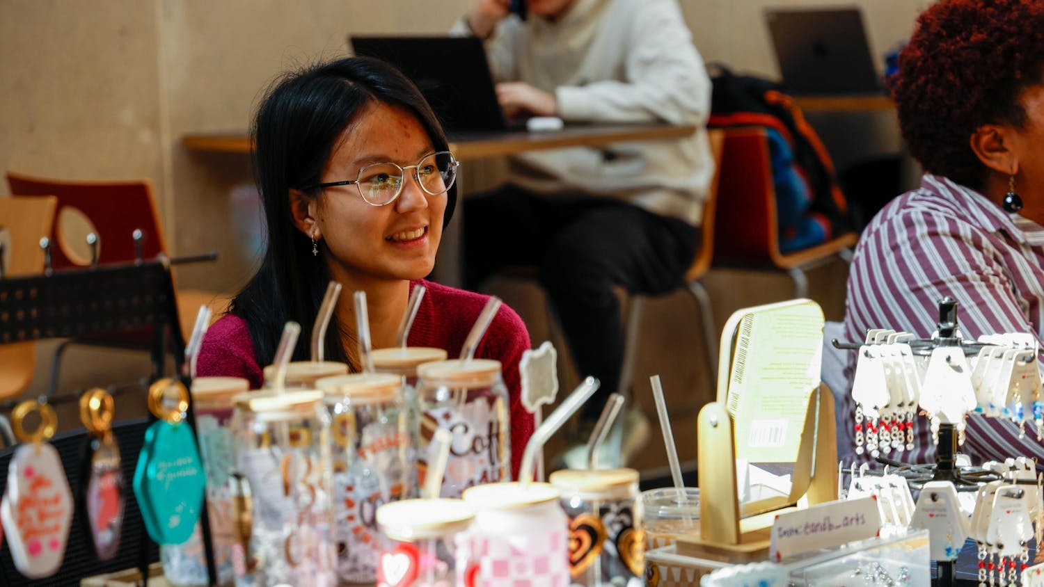Second-year anthropology student Ellie Dawkins smiles while sitting behind her booth at a tabling event for Student-Made USC in Russell House on Feb. 17, 2025. Dawkins is the owner of E&B Arts, which sells handmade jewelry and other accessories.