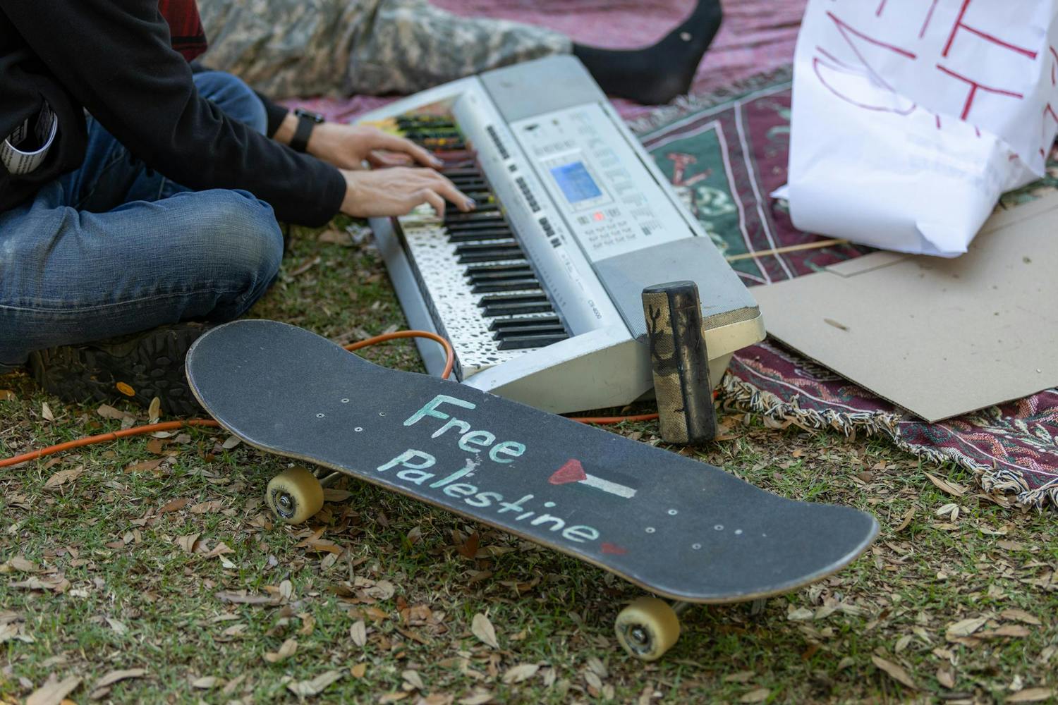 A protestor plays the keyboard next to a skateboard reading "Free Palestine" on Davis Field on April 22, 2024. Music was played by protestors via keyboard, and recorded tracks were played on a speaker at various points during the day.