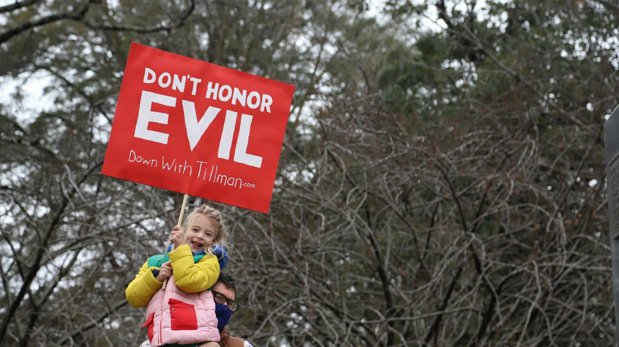 A protestor holds up a child with a sign saying “DON’T HONOR EVIL, Down with Tillman” in front of the Benjamin Tillman statue on Tuesday January 12, 2021.