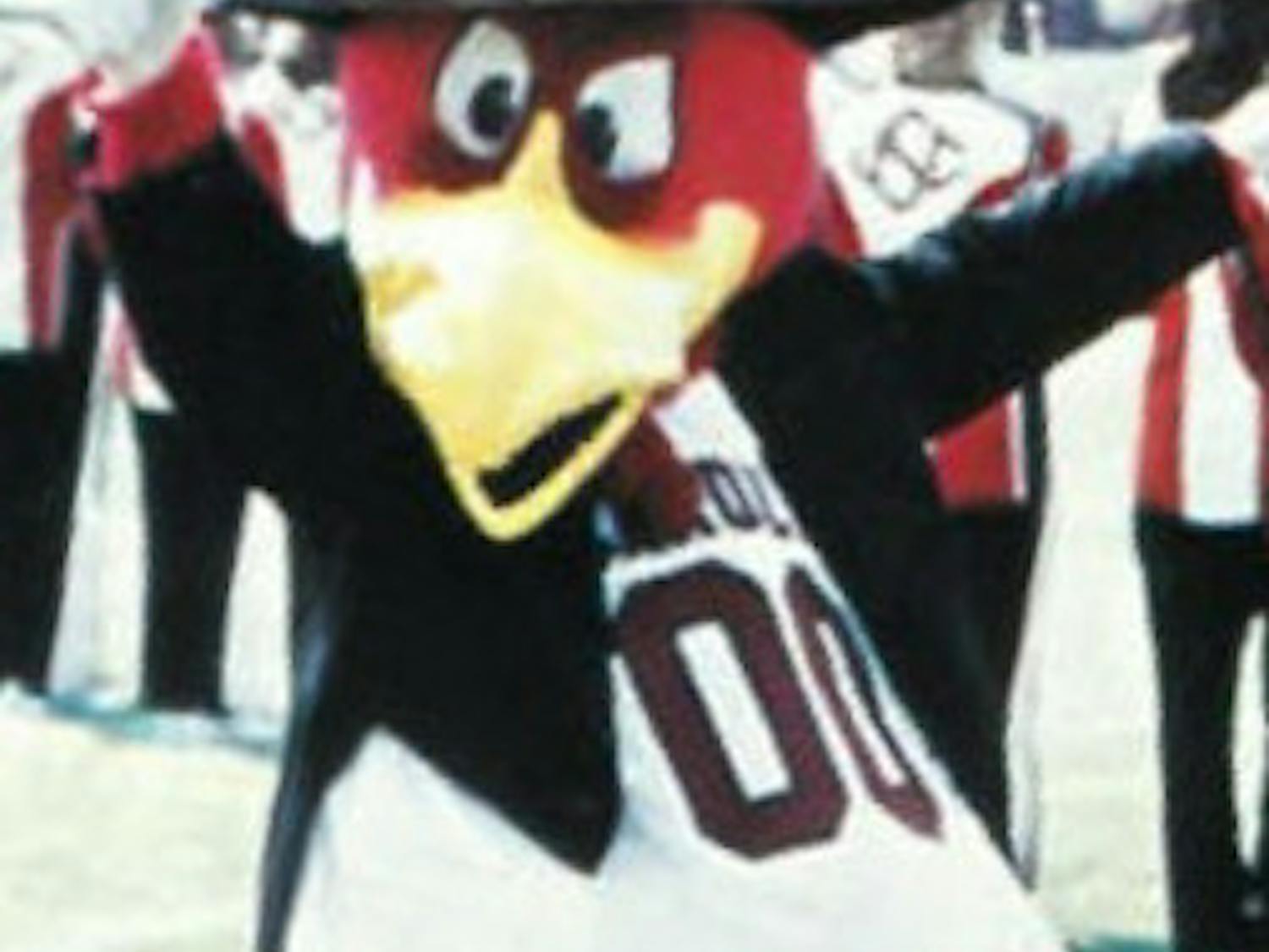 Cocky wears a top hat and suit as he cheers in front of the marching band on the football field. This moment was captured in 1985 and shows off one of many specialty outfits for Cocky.
