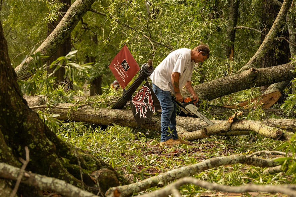 <p>A man with a chainsaw cuts branches off a tree that fell in front of DeSaussure Hall on Sept. 27, 2024. The tree fell after Hurricane Helene hit the University of South Carolina.</p>