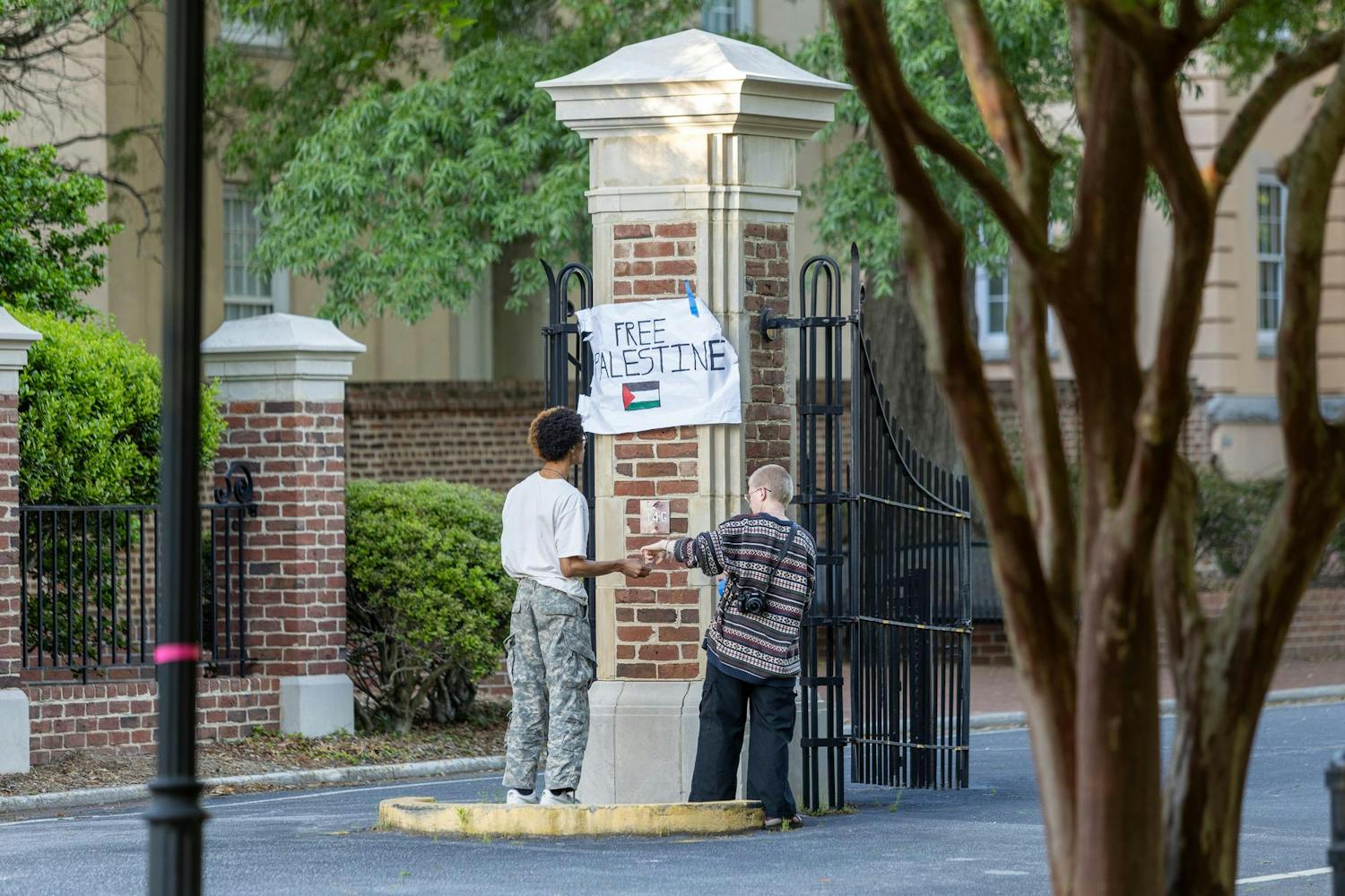 Attendees of the "Anti-Zionist Passover" tape a sign saying "Free Palestine" to the center of gates on Greene Street on April 22, 2024. Signs were taped to trees and poles surrounding Davis Field during the protest.