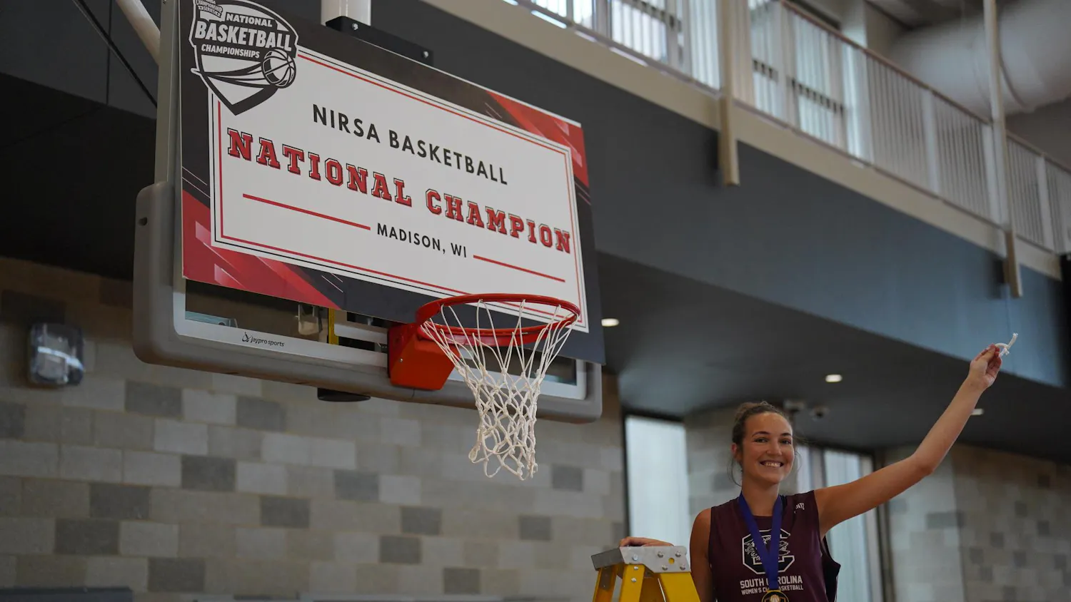 South Carolina third-year public health student Addison Marston holds a piece of basketball netting atop a ladder while posing in celebration following victory in the National Intramural-Recreational Sports Association national championship game.