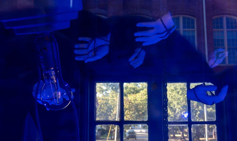 Hands hang from a ceiling under blue light on Sept. 26, 2022 in an installation by artist Brittany M. Watkins’ installation for the Mill District Public Art Trail. Watkins' installation features hands which hang from the ceiling of the guard house in her work titled ‘Hands Unseen.’