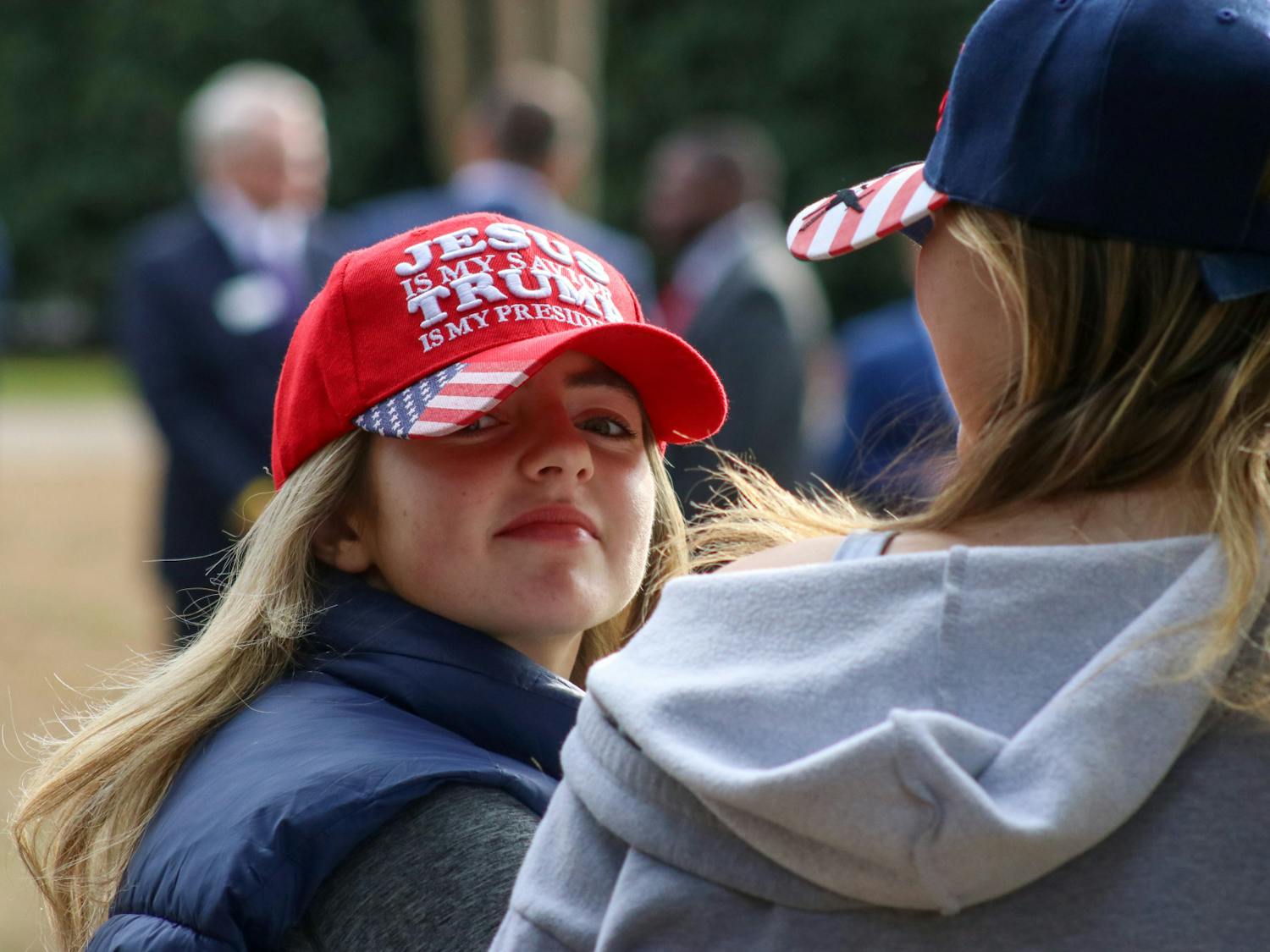 A woman (left) wears as a hat that says "JESUS is my savior, TRUMP is my president," while standing along the fence outside the Statehouse on Jan. 28, 2023. The MAGA branding of bright red and American flags could be seen across the Statehouse lawn, as former President Donald Trump's private campaign event brought many local Trump supporters back into the public eye.&nbsp;