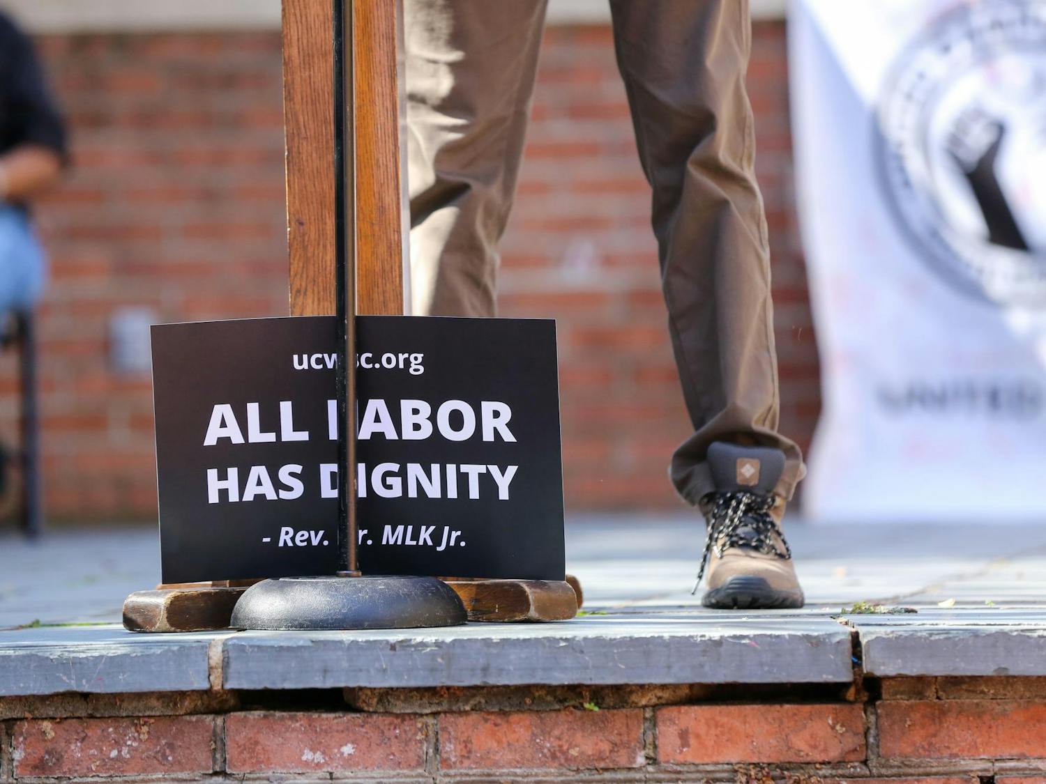 A sign of a quote by Martin Luther King Jr. stating "All labor has dignity" sits in front of the podium during a USC worker speak-out event held on the Russell House patio on Oct. 26, 2023. Employees across the university gathered to push for an increase in minimum wage.
