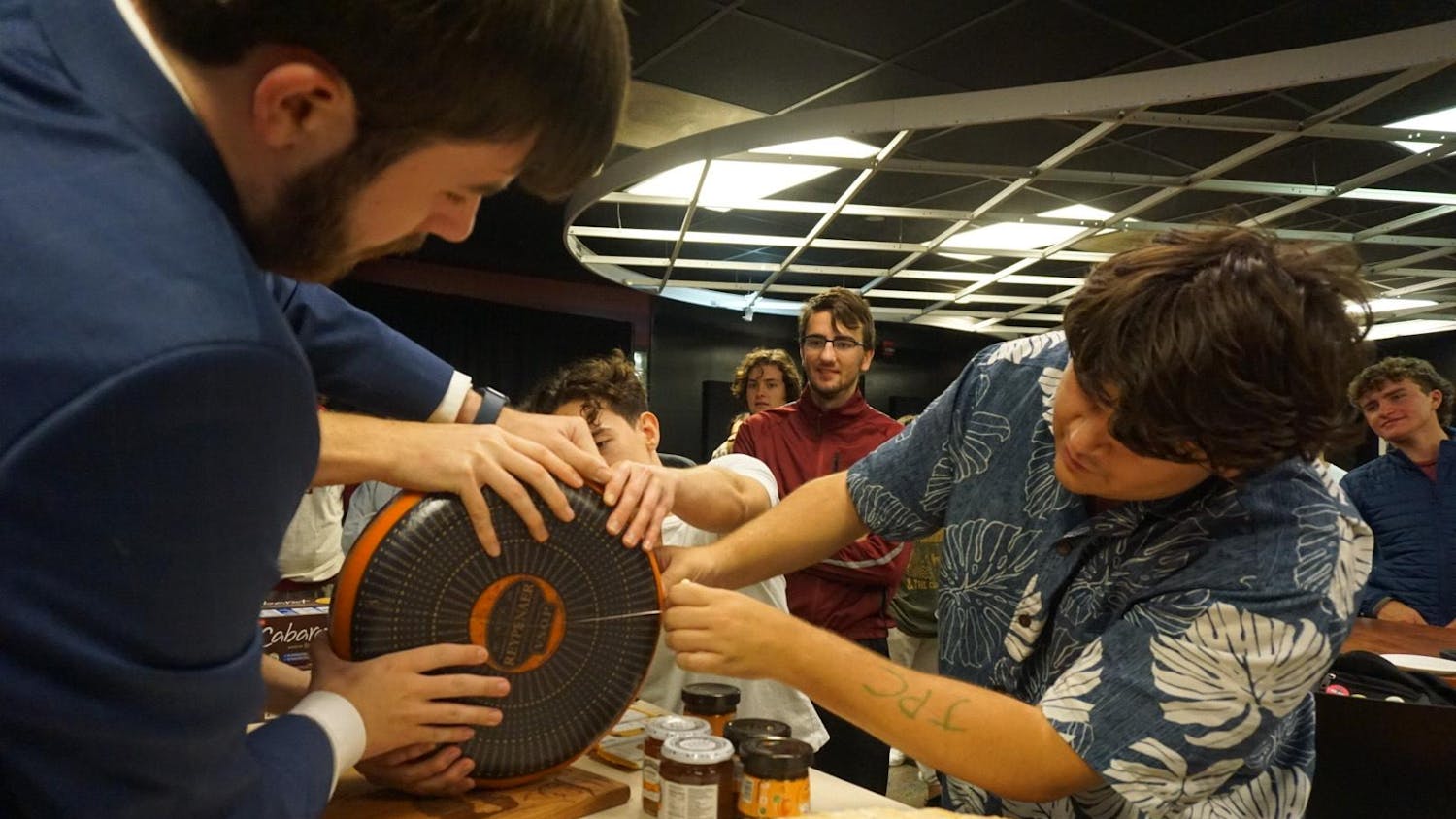 Jesse Pinkman Conglomerate President Ash Jacobson and second-year music industries student Scott Manning attempt to cut a wheel of gouda cheese with a wire during a "Cheese Wheel" event held in the Russell Underground on Nov. 22, 2024. The Jesse Pinkman Conglomerate hosted the event and invited students try a 28-pound wheel of cheese along with other food and refreshments.