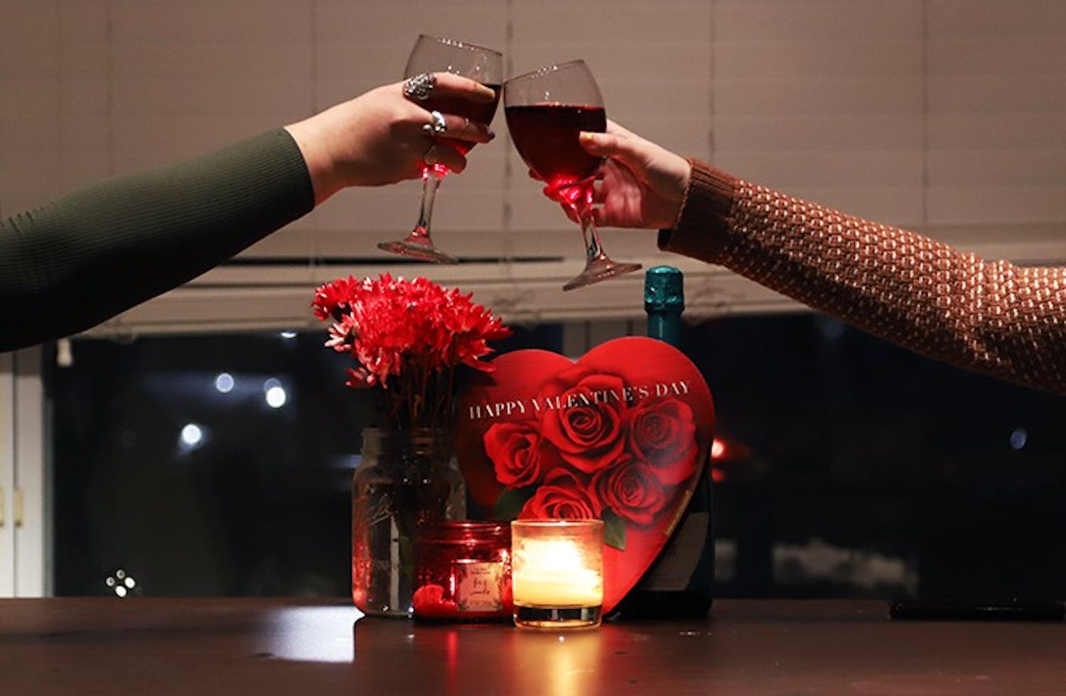 Two girls clink their glasses together with Valentine's Day paraphernalia behind them.
