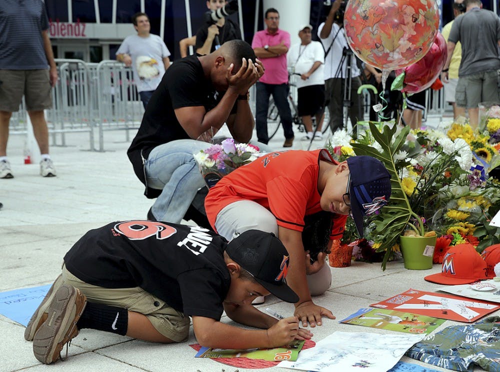 Fans Peyton Holton (front) and Shawn Lopez pay tribute by signing posters at a memorial for Miami Marlins&apos; pitcher Jose Fernandez, who died on a boat accident Sunday morning, on Monday, Sept. 26, 2016 at Marlins Park in Miami, Fla. (Pedro Portal/Miami Herald/TNS)