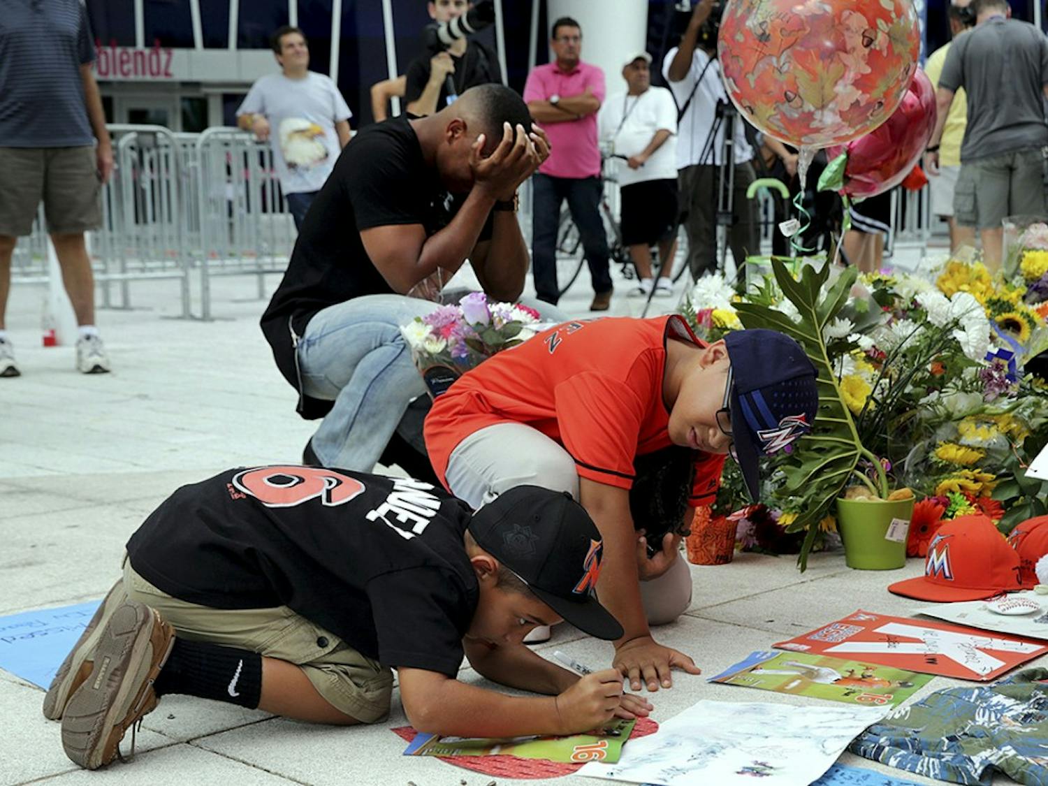 Fans Peyton Holton (front) and Shawn Lopez pay tribute by signing posters at a memorial for Miami Marlins' pitcher Jose Fernandez, who died on a boat accident Sunday morning, on Monday, Sept. 26, 2016 at Marlins Park in Miami, Fla. (Pedro Portal/Miami Herald/TNS)