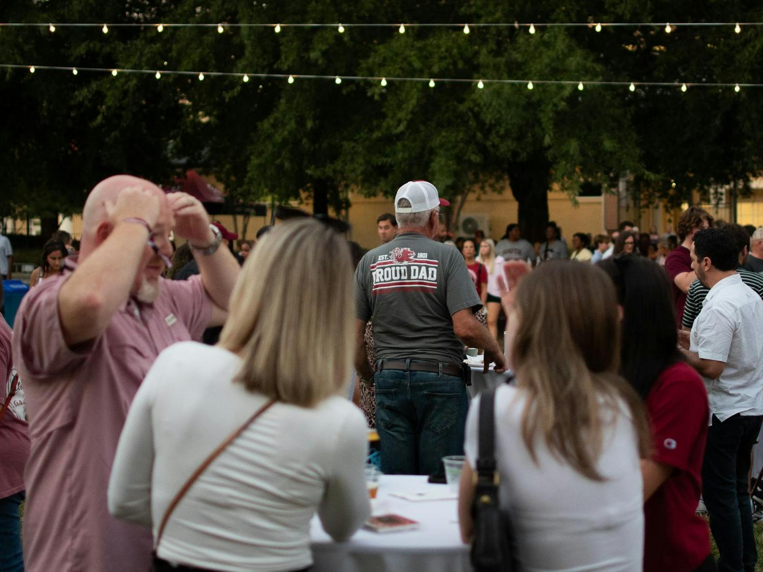 A man wearing a USC-themed "Proud Dad" shirt stands at a table with other visitors outside the Strom Thurmond Wellness and Fitness Center on Sept. 20, 2024. The Wellness and Fitness Center hosted the 'Rock the Roost' Family Weekend event.