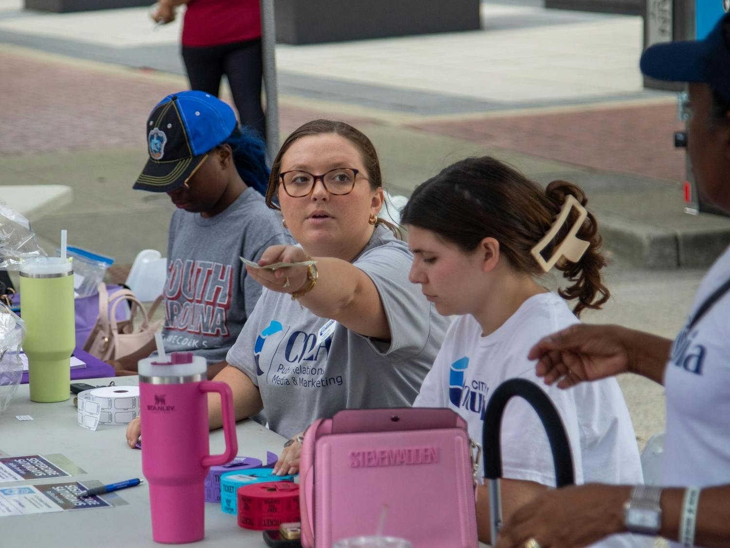 A volunteer from the City of Columbia Public Relations and Media Marketing hands money to another volunteer at Soda City Market on July 27, 2024. The City of Columbia was one of the organizations that participated in Sistercare Saturdays.
