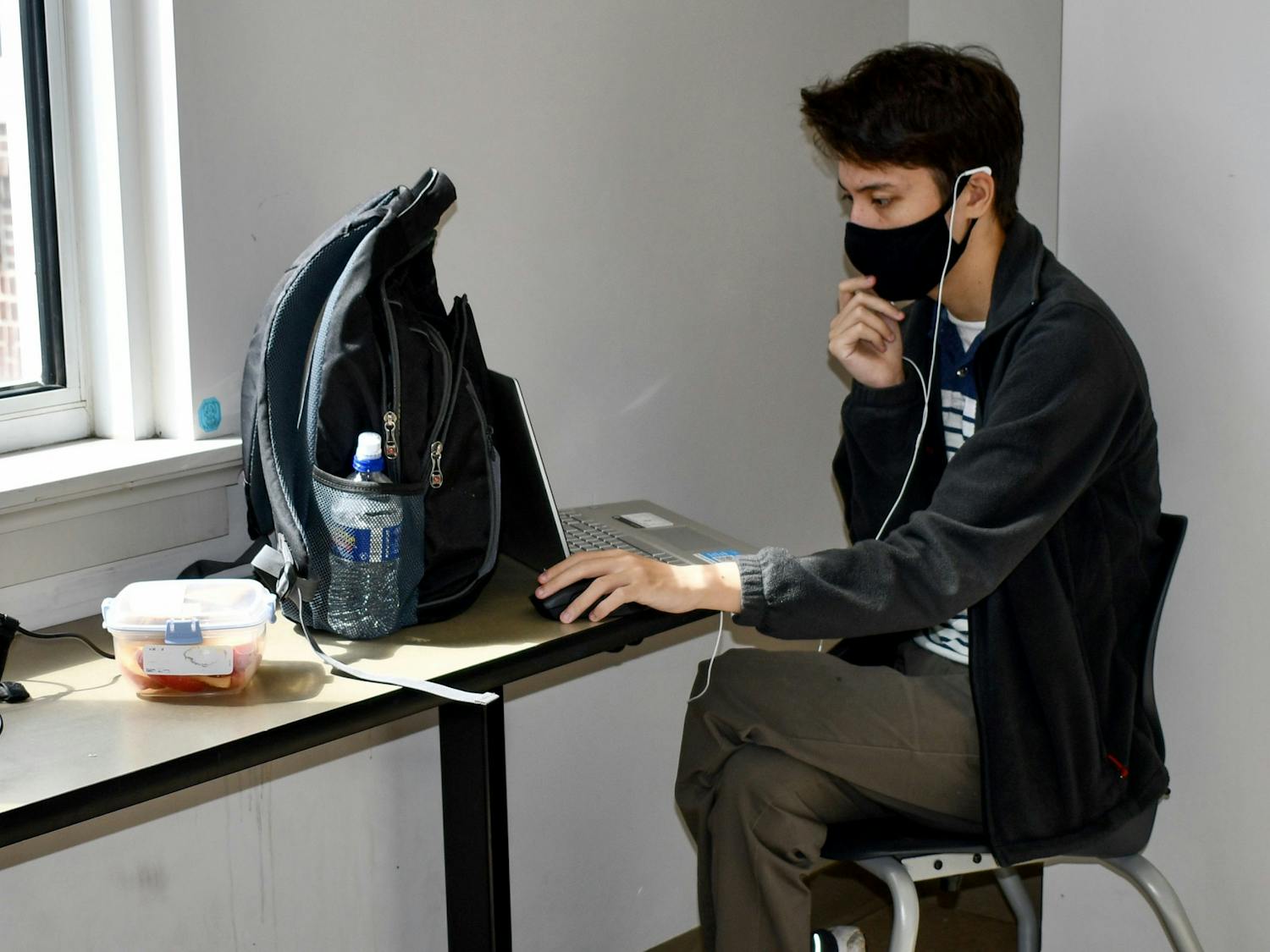 A student works virtually on his computer. All students are required to wear a mask while on campus.