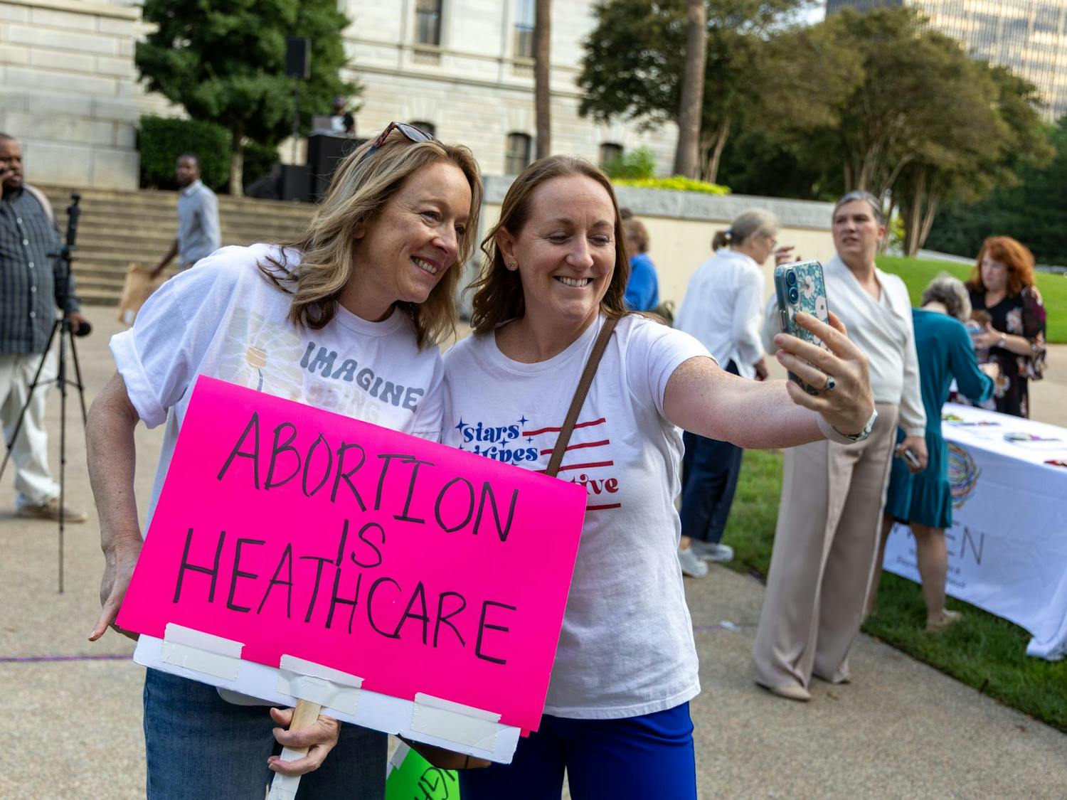Two women take a photo together while holding up a pink sign reading "ABORTION IS HEALTHCARE" during a protest against S.B. 323 on the lawn of the SC State House on Oct. 1, 2025. In addition to banning abortion after six weeks, the bill would also make abortion a felony equivalent to “the homicide of a person born alive."