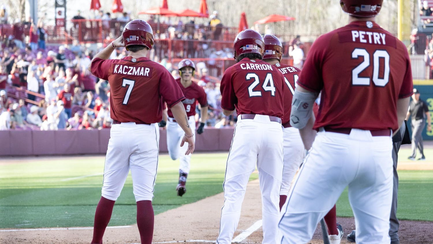 Three University of South Carolina players await their teammates crossing home plate after scoring a run during their matchup against Morehead State at Founders Park on March 8, 2025. The Gamecocks won 16-11.