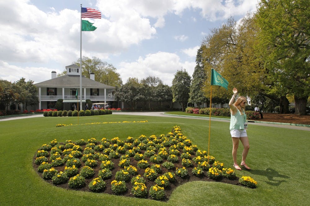 A patron poses for photos next to the Masters logo in flowers at Founders Circle in front of the Augusta National clubhouse in Augusta, Georgia, during a practice round for The Masters, Monday, April 8, 2013. (Gerry Melendez/The State/MCT)