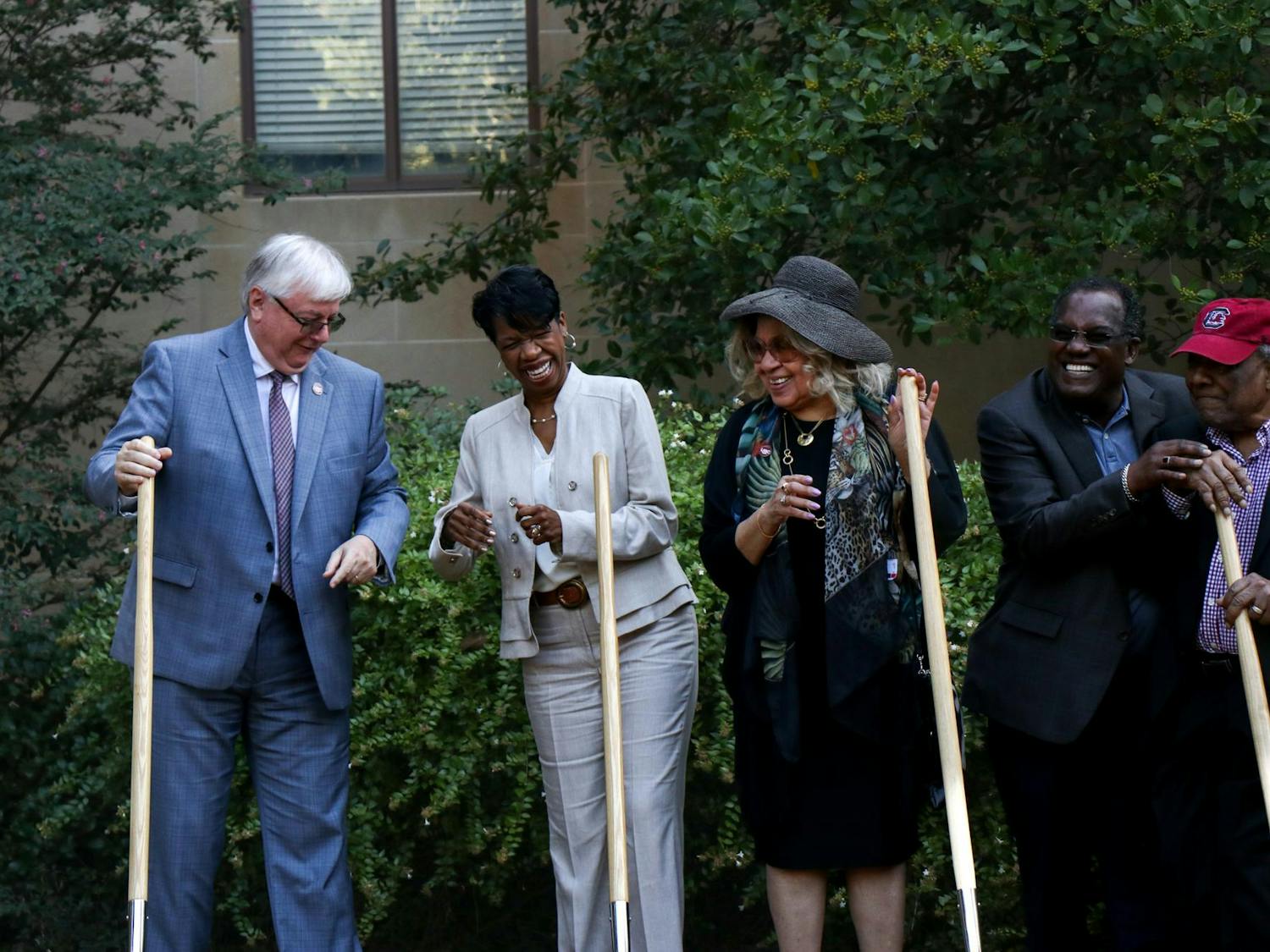 USC President Michael Amiridis (left), Cindy Baumgardener (center) and Henrie Monteith Treadwell (right) smile while breaking ground where a monument will be placed in 2024 to honor the first three Black students to graduate from USC. A sign showing Treadwell, Anderson and Solomon Jr. now stands outside of McKissick Museum.