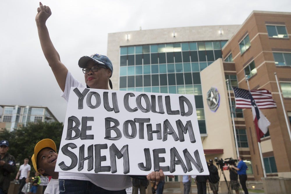 Dr. Pamela Grayson raises her fist as "Young King" Solomon Grayson, 6, peaks behind her sign during a Mothers Against Police Brutality candlelight vigil for Botham Shem Jean at the Jack Evans Police Headquarters on Friday, September 7, 2018, in Dallas. Botham Shem Jean was shot by a Dallas police officer who mistook his apartment for hers on Thursday night. (Shaban Athuman/Dallas Morning News/TNS) 