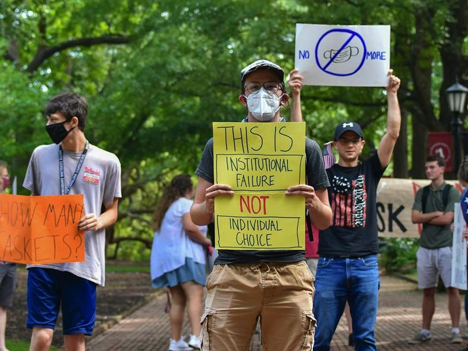 Two members of Carolina Socialists stand on the Horseshoe, holding signs while a member of the USC Turning Point USA chapter stands behind them with an anti-mask poster. Turning Point USA protested the mask mandate outside the President's House, and the Carolina Socialists counterprotested the anti-mask messages.