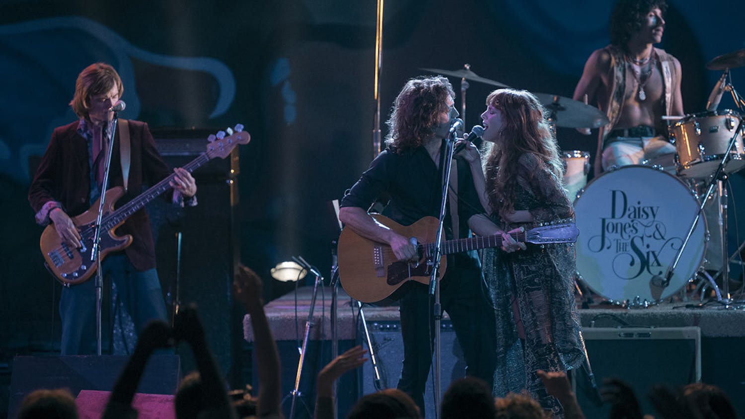 Sam Claflin (center) and Riley Keough (right) sing together during a scene from the drama miniseries, &nbsp;"Daisy Jones &amp; The Six." The series is a live-action adaptation of American author Taylor Jenkins Reid's novel by the same name, and it follows the lives of a fictional 1970s rock band from the perspective of their older selves.&nbsp;