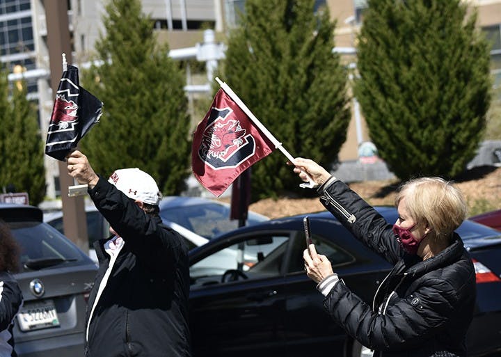 Two fans wave Gamecock flags toward the approaching procession of players.