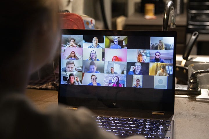 A person sits in their kitchen while watching a pre-recorded Zoom lecture.
