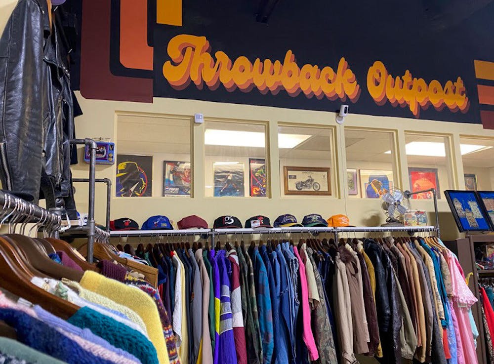 <p>A rack of vintage clothes sit in front of a sign painted by Nicolette Bryan at Throwback Outpost on Feb. 7, 2023. The store, located on North Beltline Boulevard in Columbia, S.C., houses a plethora of vintage items from clothes, to records and even custom rugs.</p>