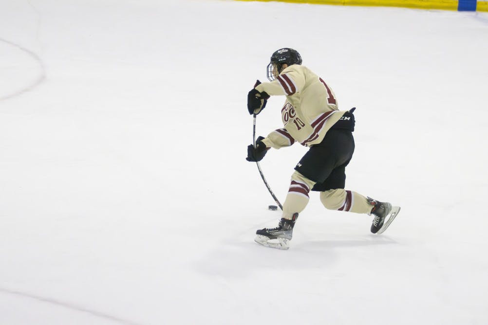 A player is in stride with his hockey stick bending with him as he hits the puck on the ice. 