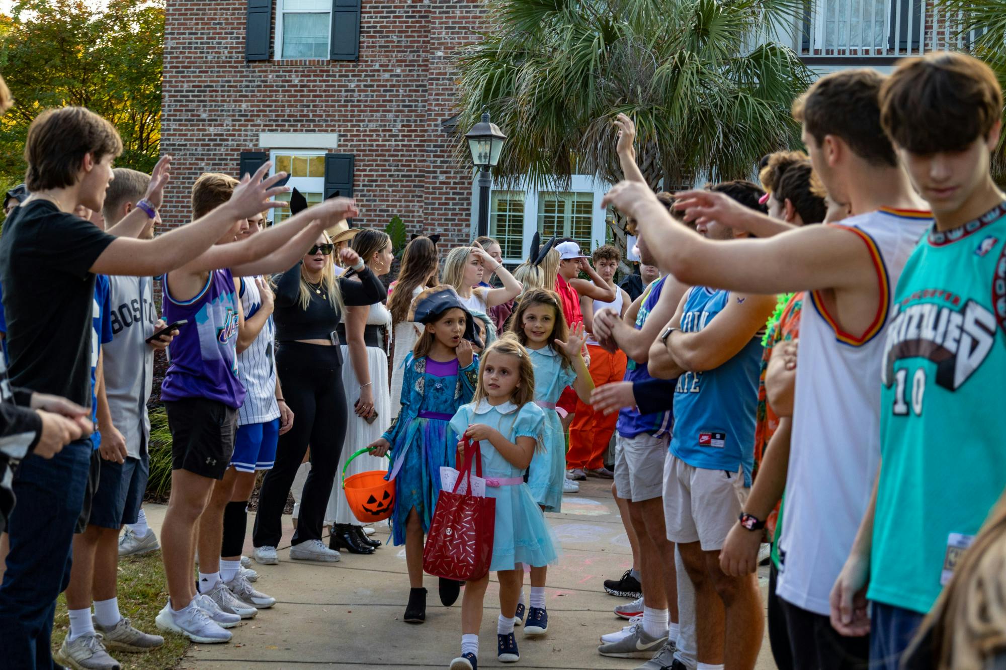 USC fraternity members salute a group of young trick or treaters as they walk down a pathway in USC's Greek Village on Oct. 25, 2022. USC fraternities and sororities celebrated Halloween with community members during their community outreach event.