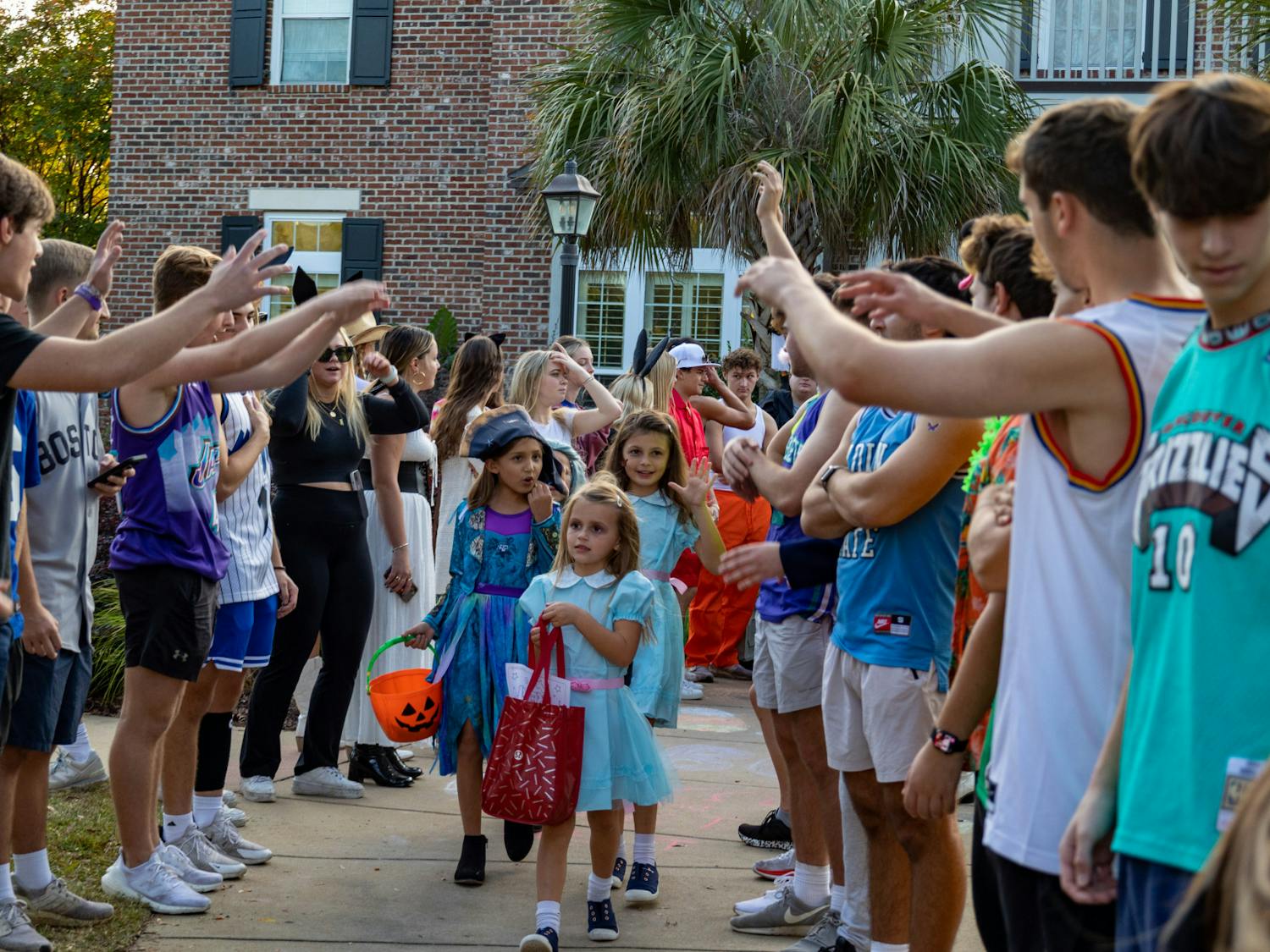 USC fraternity members salute a group of young trick or treaters as they walk down a pathway in USC's Greek Village on Oct. 25, 2022. USC fraternities and sororities celebrated Halloween with community members during their community outreach event.