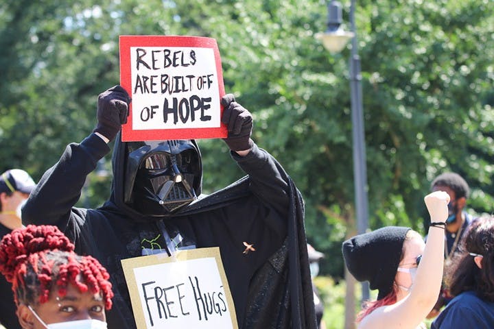 Dressed in a Darth Vader costume, a protester stood on the side of the street in front of the Statehouse holding a sign that references "Rogue One: A Star Wars Story."
