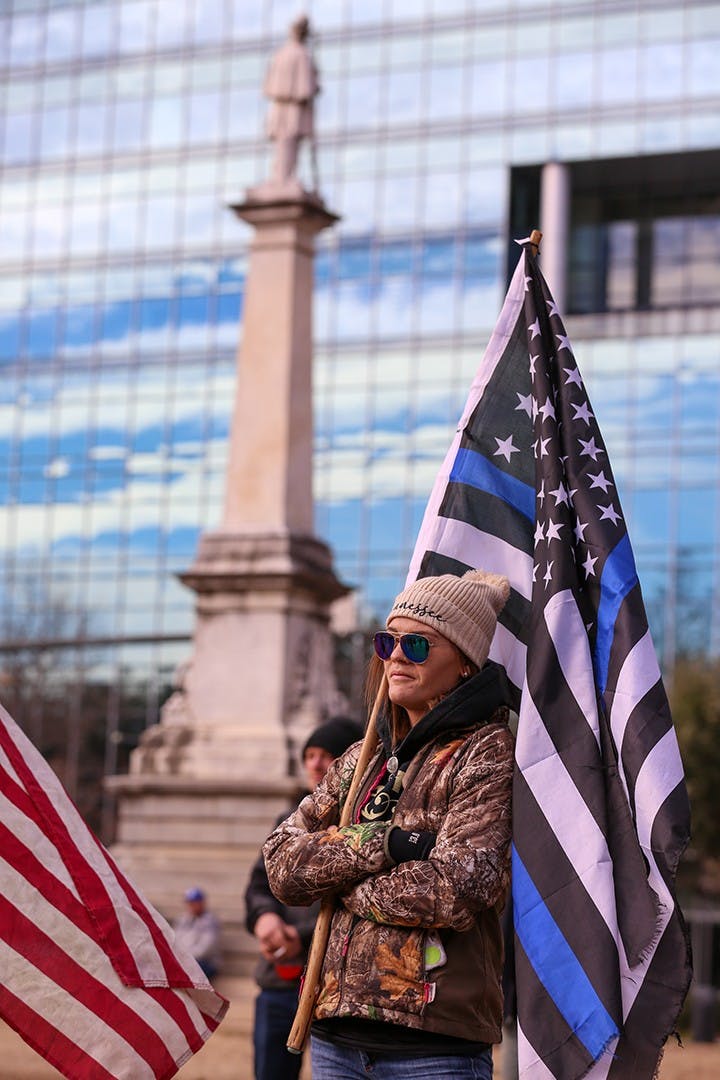 A member of the “Drive4America” caravan holds a Blue Lives Matter flag in front of the Statehouse while listening to a speaker.&nbsp;