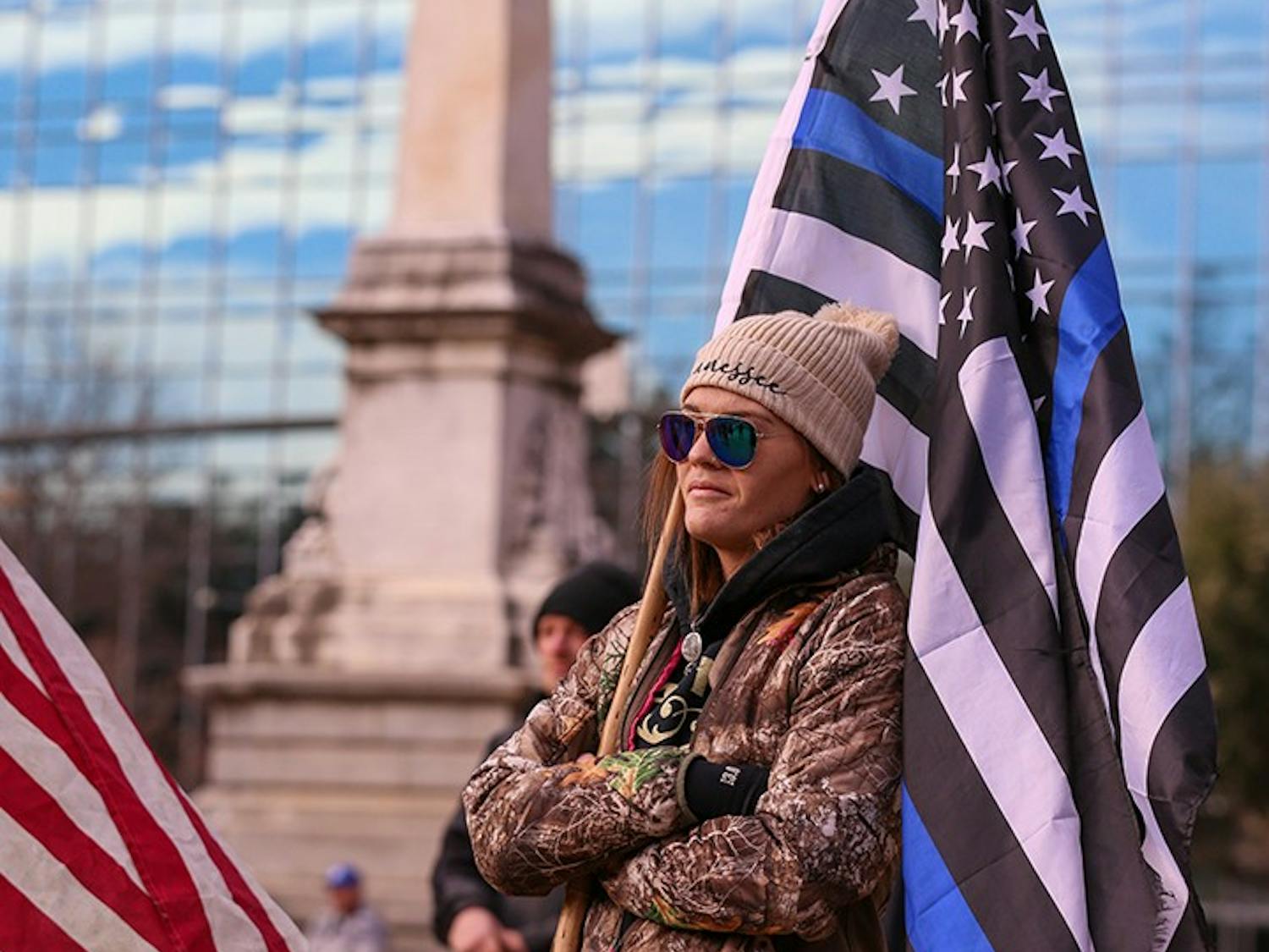 A member of the “Drive4America” caravan holds a Blue Lives Matter flag in front of the Statehouse while listening to a speaker.&nbsp;
