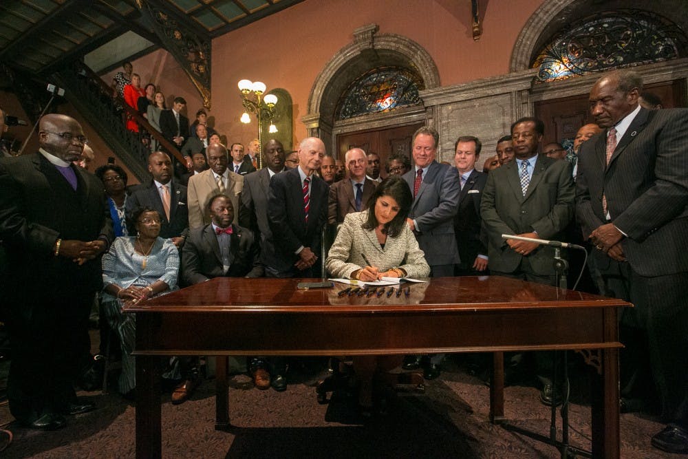 South Carolina Gov. Nikki Haley, surrounded by three former governors, some family members of the slain nine and many legislators, signs the bill to remove the Confederate flag from the South Carolina State House grounds on Thursday, July 9, 2015, in Columbia, S.C. (Tim Dominick/The State/TNS)