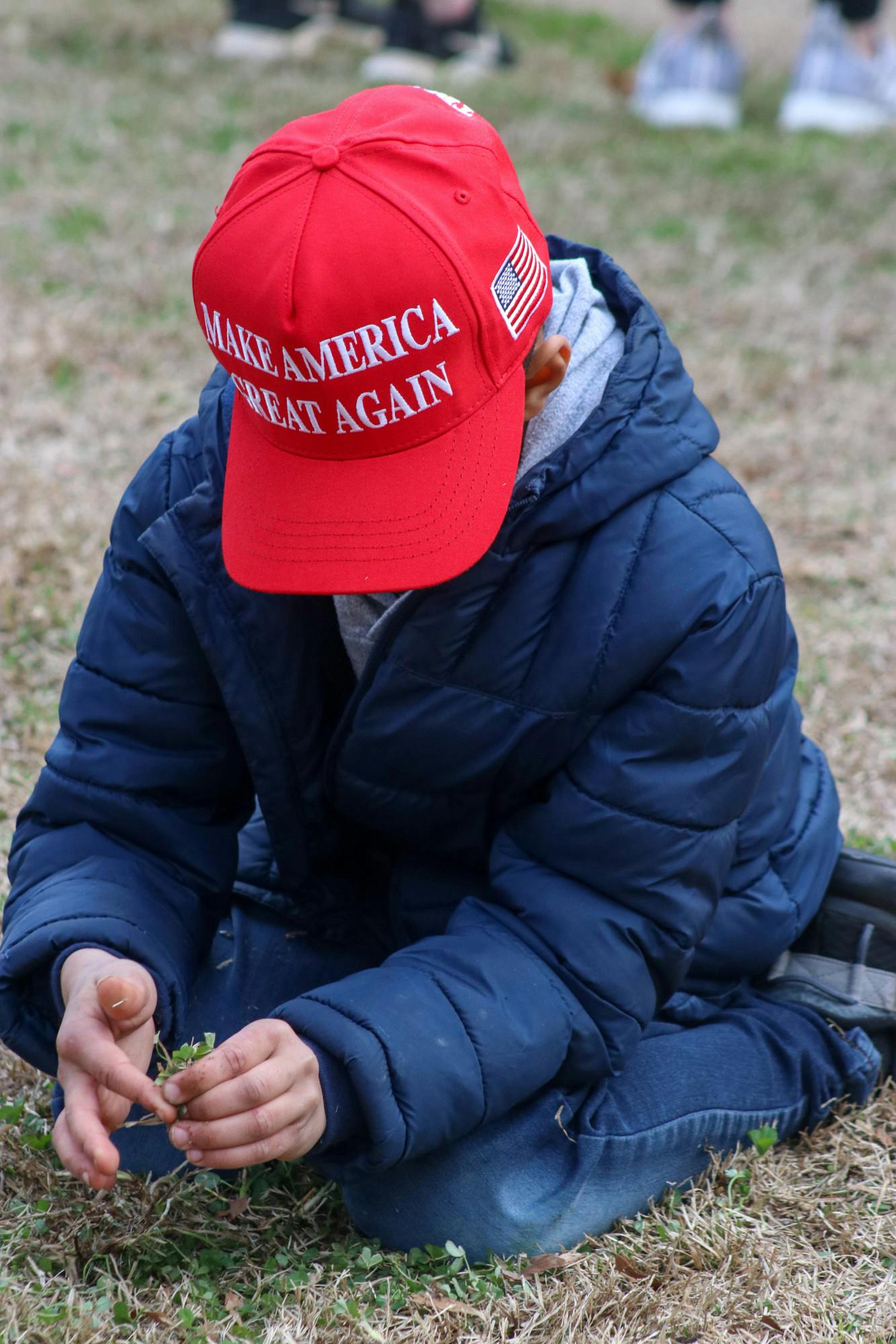 A child plays with grass while waiting outside of the Statehouse during Trump's first campaign visit on Jan. 28, 2023. Some children wore MAGA merchandise while standing with their families on the Statehouse lawn.&nbsp;
