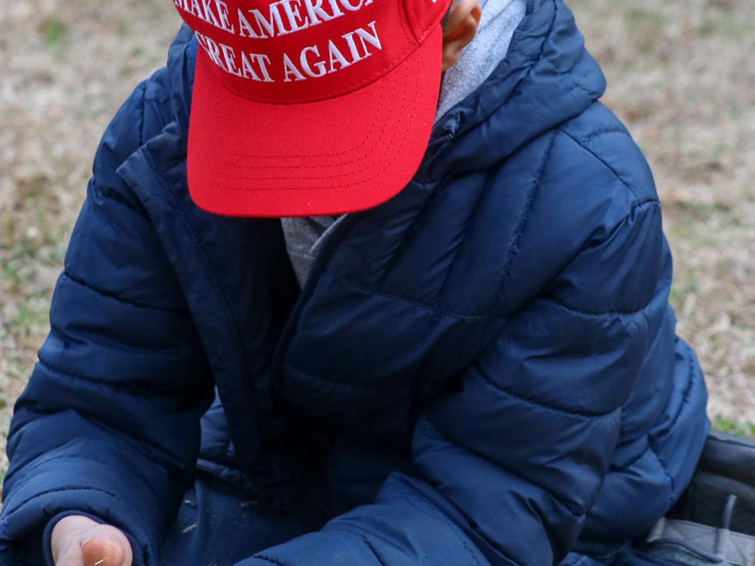A child plays with grass while waiting outside of the Statehouse during Trump's first campaign visit on Jan. 28, 2023. Some children wore MAGA merchandise while standing with their families on the Statehouse lawn.&nbsp;